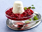 Goat cheese and honey ice cream with raspberry sauce and mint in glass cake stand