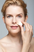 Close-up of gray eyed woman applying make-up with sponge on her face