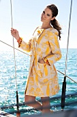 Frau steht, Mantel gemustert, gelb- weiß, Segelboot, Kamerablick