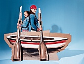 Side view of mother and daughter standing back to back behind sailboat made of cardboard