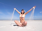 Woman wearing bikini playing with sand on beach, smiling