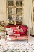 Sofa with scatter cushions on white wooden floor in front of lattice window with peeling frame