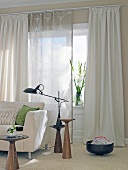 Lamp and sofa in front of window with beige curtains in living room