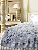 Close-up of bed with blue and white striped linen bed sheet and crochet blanket