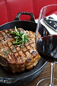 Close-up of rib eye steak with rosemary in casserole and glass of red wine