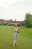 Blonde woman wearing top and checked pant holding bucket of golf balls, smiling