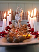Close-up of wooden tray decorated with silver reindeer, lit candles and walnuts