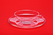 Glass cup with saucer on red background