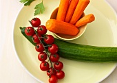 Carrots in bowl with bunch of tomatoes and cucumber on plate