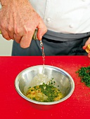 Close-up of man's hands pouring vinaigrette in bowl with pine nuts