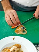 Close-up of man's hands cutting mussel meat with knife on cutting board