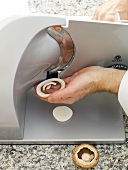Close-up of man's hands cutting mushroom into thin slices in slicer
