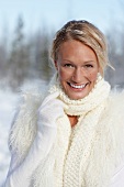 Portrait of cheerful blonde woman wearing woollen scarf with snow in hair, smiling