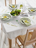 Table with embroidered table cloth, plates, napkins and salad