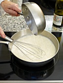 Fish with white wine sauce being whisked while cooking in pan