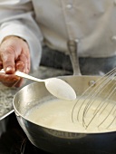 Close-up of fish with white wine sauce mixture being whisked in pan