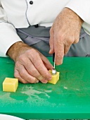 Potato cubes being scooped on chopping board