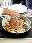 Adding beef steak to vegetables in pan