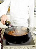 Pouring red wine to ingredients of beef sauce in frying pan