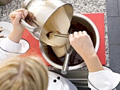 Adding cream to chocolate mixture in bowl with whisk