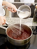 Adding milk to mixture in saucepan with whisk