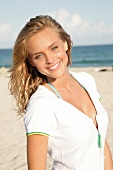 Portrait of young blonde woman wearing white zipper standing on beach, smiling