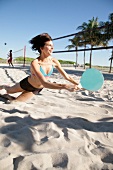 Woman with dark hair wearing bikini playing board racket game on beach, blurred motion