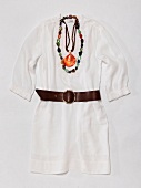 Close-up of white tunic, leather belt, necklaces with gemstone and shell