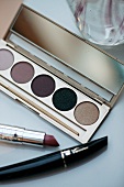 Close-up of lipstick, mascara and various eye shadows in a palette on white background