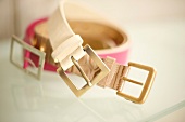 Close-up of belts in fuchsia and ivory with brass buckle