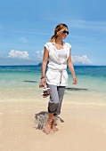 Frau mit Sonnenbrille in Hose und Baumwollbluse, Spaziergang am Meer
