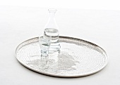 Glass of water with carafe on round aluminium tray