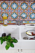 Basil sprigs and vegetables in a white ceramic sink with Moroccan tiles on the wall behind