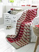 Strickplaid lies over white armchair beside drawer with cushion