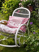 A rocking chair in a summery garden with a decorative, embroidered cushion