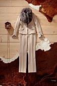 Beige trouser suit with fur collar and small wall clock on wooden floor