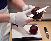 Close-up of man's hand wearing gloves and peeling beetroot with knife