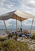 Outdoor-Möbel: Gartentisch mit aufge stecktem Sonnendach am Strand