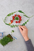 Ernährungs-Check: Hand formt Auge aus Tomaten, Kresse und Rucola
