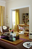 View of living room with wooden table, white chair, glass table and flower vase