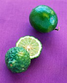 A lime and a kaffir lime on a purple surface