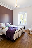 Schlafzimmer mit Metallbett vor lilafarbener Wand in Altbauwohnung