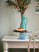 Chocolate cake with cream and sugared sea buckthorn berries on glass cake stand