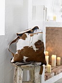 A cowhide backpack on a rustic wooden stool next to a wall niche with candles