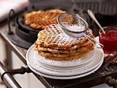 A sieve of icing sugar on top of a stack of cinnamon waffles