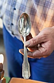 Close-up of man's hand holding silver spoon