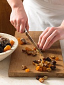 Fruits being cut into small pieces with knife for preparation of fruit cake, step 1