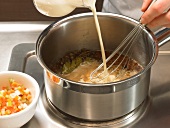 Milk being added to mixture in saucepan while preparing beer sauce, step 1