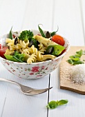 Pasta with spring vegetables in bowl on white surface