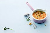 Tomato and coconut soup in pot with spoon on white background